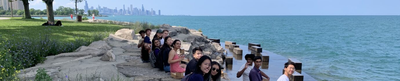 A group of students sitting by Lake Michigan with the Chicago skyline in the background